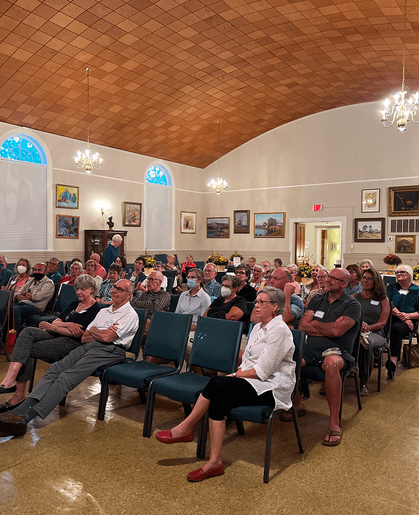 Audience seated in ornate community meeting hall