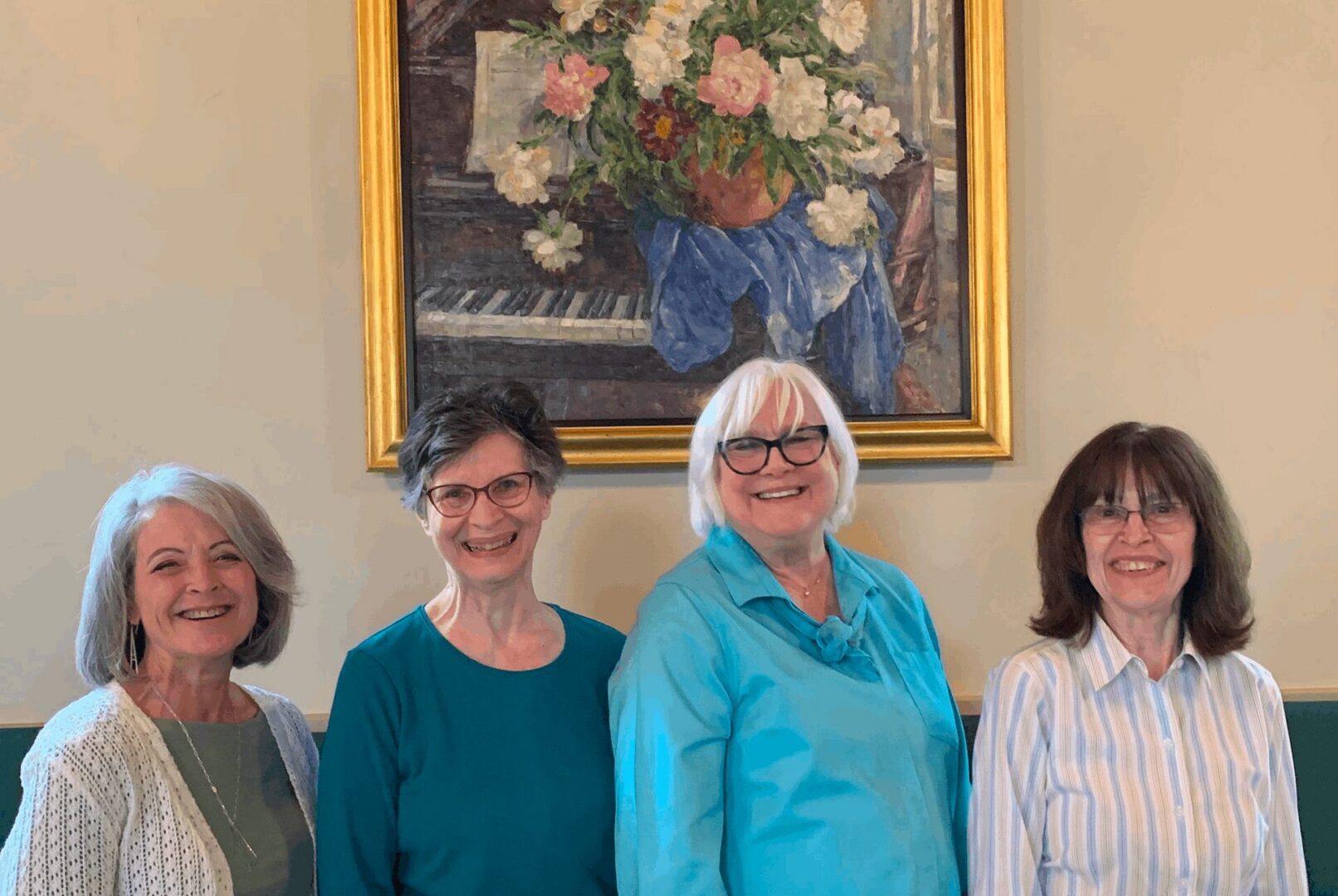 Four smiling women standing before framed floral painting